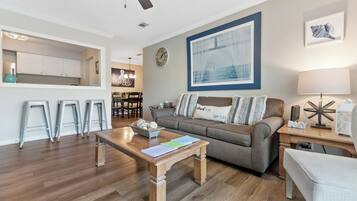 A living room with a sofa, coffee table, and a dining area with stools.
