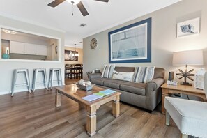 A living room with a sofa, coffee table, and a dining area with stools. - Water View - optional BIKES - Walk 2 Pier Village (St. Simons Island)