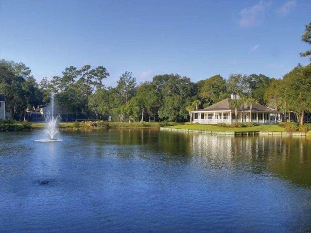 A tranquil lake with a fountain, surrounded by lush greenery and a pavilion.