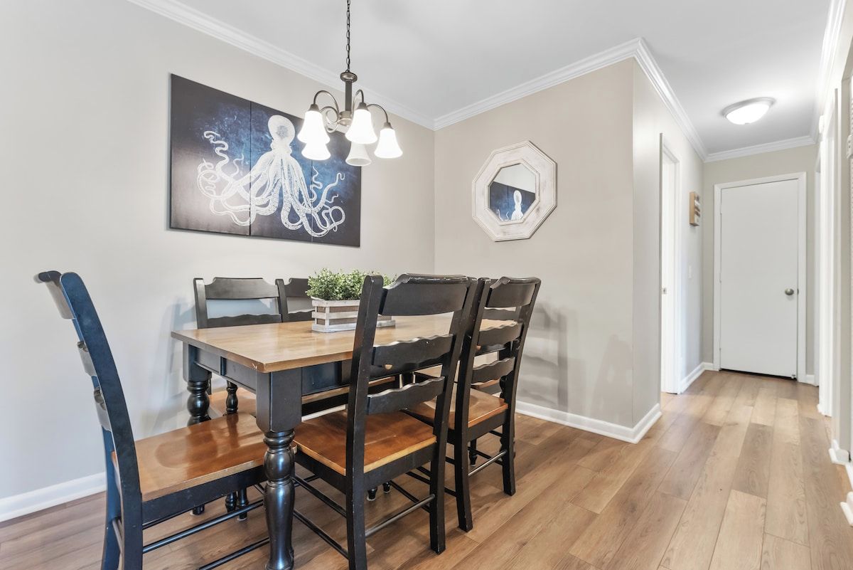 A dining area with a wooden table and chairs, a chandelier, and artwork on the wall.