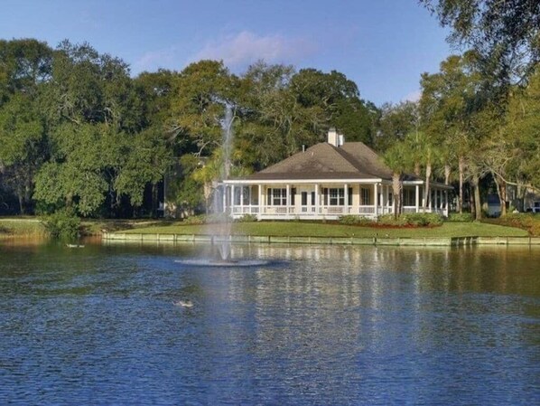 A house with a large porch overlooking a body of water, surrounded by trees.