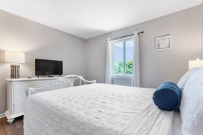 A bedroom with a bed, a TV on a dresser, a window with curtains, and a wall-mounted picture. - Water View - optional BIKES - Walk 2 Pier Village (St. Simons Island)