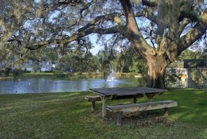 A picnic table by a lake with a fountain, surrounded by trees and a grassy area. - Water View - optional BIKES - Walk 2 Pier Village (St. Simons Island)