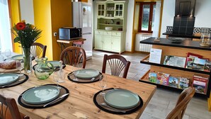 A dining area with a wooden table set for four, a kitchen in the background, and a small cabinet with glass doors.