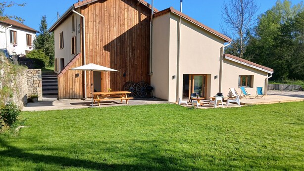 A two-story house with a wooden exterior, a patio with a table and chairs, and a lawn.