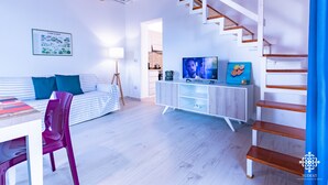 Un salon moderne avec un escalier, un canapé, un téléviseur et un coin repas.