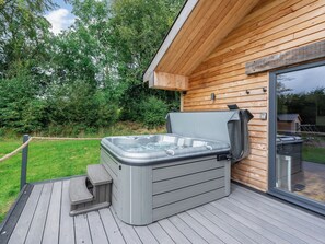 Een hottub op een houten terras, met een glazen deur naar een overdekt terras.