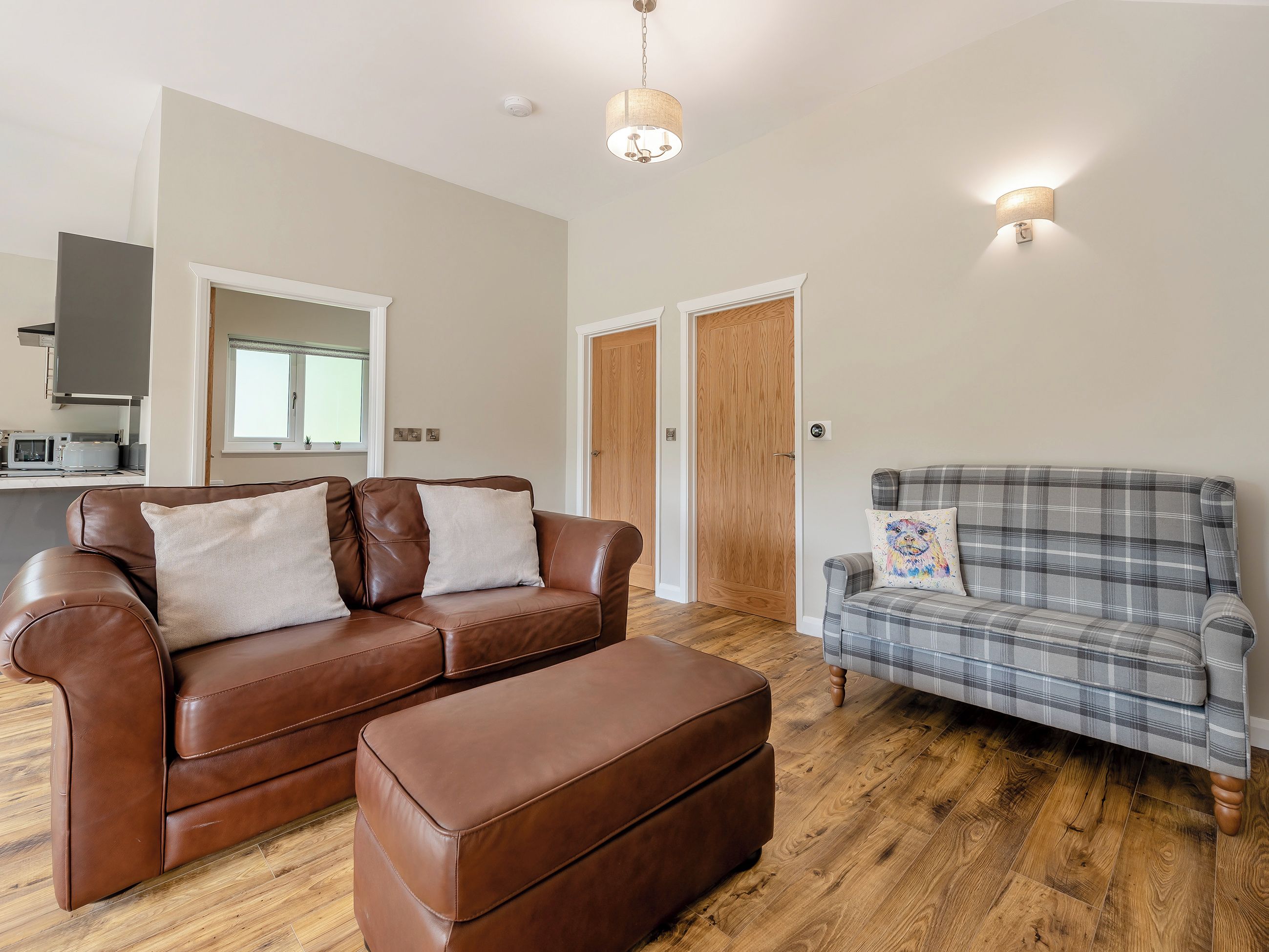 A living room with a brown leather sofa, a plaid sofa, and a wooden floor.