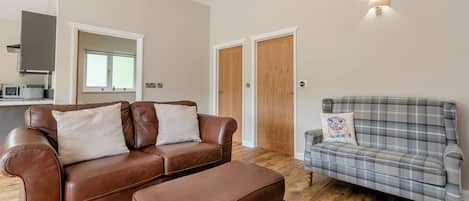 A living room with a brown leather sofa, a plaid sofa, and a wooden floor.