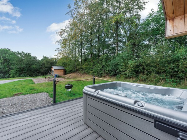 A hot tub on a wooden deck with a view of a forest and a small building in the background.