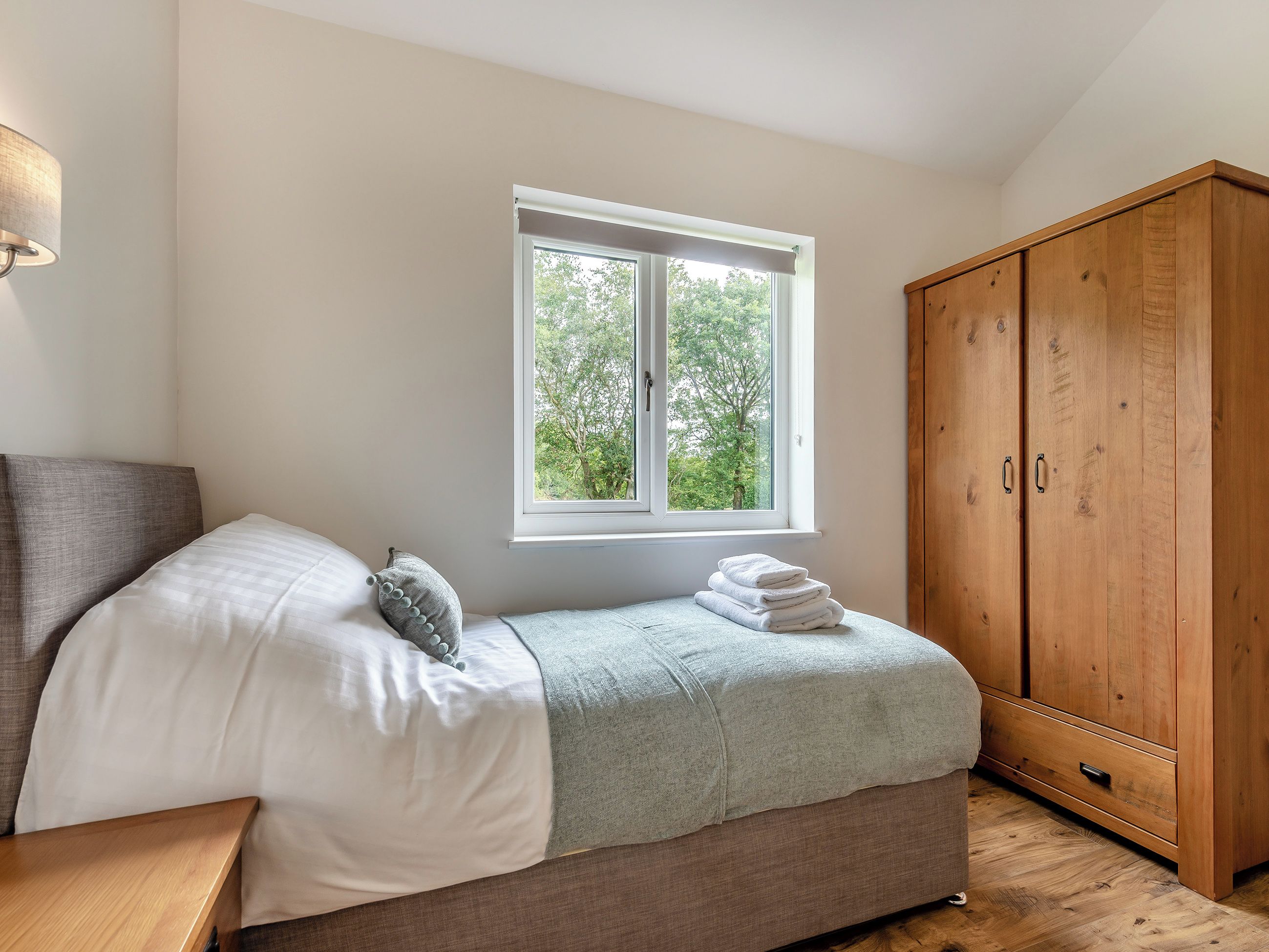 A bedroom with a bed, a window with a view of trees, and a wooden wardrobe.