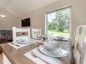 A dining table set with white plates, bowls, and glasses, with a window view of a garden.