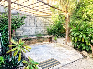 Relax in a serene garden setting surrounded by lush greenery and a pergola.