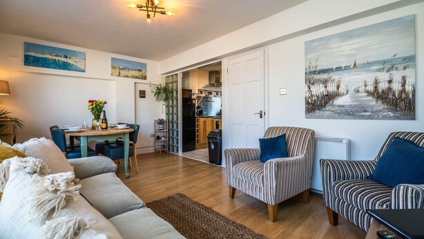 Ein geräumiges Wohnzimmer mit einer Couch, Sesseln, einem Esstisch und Kunstwerken an den Wänden.