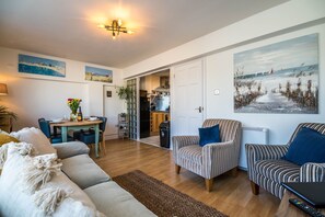 Un salon spacieux comprenant un canapé, des fauteuils, une table à manger et des œuvres d’art accrochées aux murs.