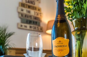 Een fles Prosecco met etiket, een glas en een decoratief bord aan de muur.
