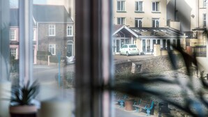 Blick auf das Gower Hotel mit einem weißen Auto vor der Fassade, einer Steinmauer und einer Bank mit Mülleimer.