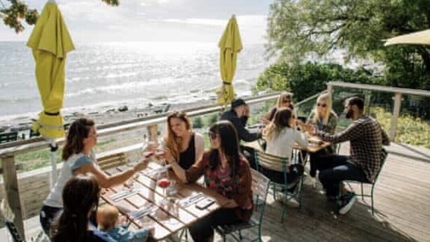 A group of people seated at an outdoor table with a view of the ocean. - Upscale Cottage - Sandbanks/Prince Edward County (Prince Edward)