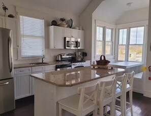 Una cocina con armarios blancos, una isla central con taburetes de bar, un microondas y una estufa.