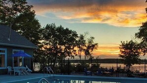 A swimming pool with a sunset view, surrounded by trees and a fenced area with lounge chairs. - Upscale Cottage - Sandbanks/Prince Edward County (Prince Edward)