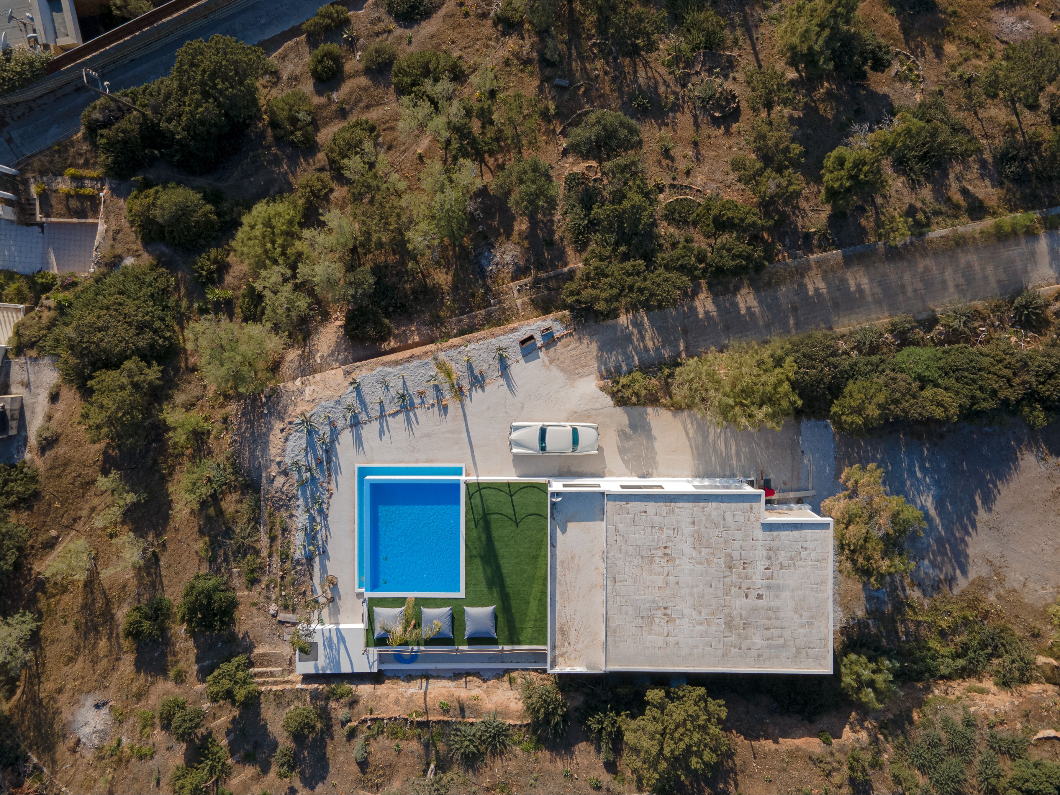 Vista aérea de una propiedad en una ladera con piscina, un patio cubierto y un edificio grande de color blanco con fachada de ladrillo.