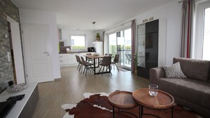 En moderne stue med sofa, spiseplads med stole og et køkken i baggrunden.