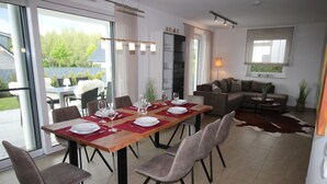 Et spiseområde med et træbord dækket til fire personer, omgivet af stole. Der er en sofa og et lille sofabord i baggrunden.