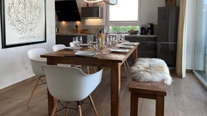 Un coin repas moderne avec une table en bois dressée pour six personnes, des chaises blanches et un plaid en fourrure sur un banc.