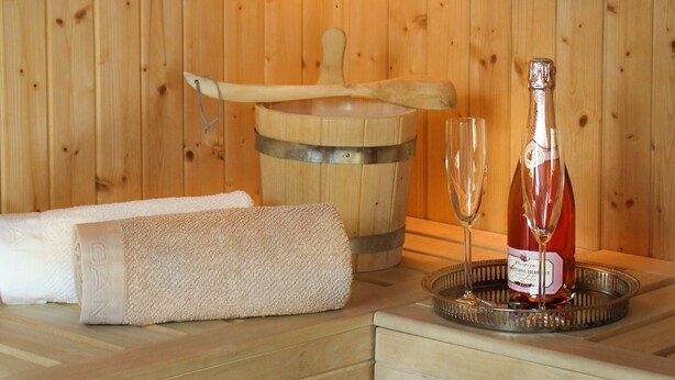 Un sauna en bois avec un banc en bois, une serviette, un seau en bois et une bouteille de vin sur un plateau.