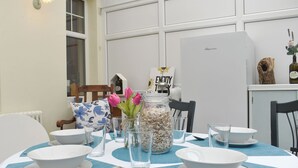 Mesa de comedor dispuesta con cuencos blancos, cucharas y vasos transparentes, rodeada de sillas.