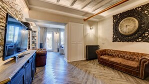 A spacious living area with a wooden herringbone floor, a leather sofa, a television, and a large ornate clock on the wall. - DesenzanoLoft : La Vite Luxury Appartment 1 (Desenzano del Garda)