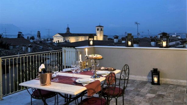 Eine Dachterrasse mit Esstisch, mit Blick auf eine Stadtlandschaft mit historischen Gebäuden und einem Turm.