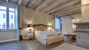 Ein Schlafzimmer mit einem großen Bett, Holzboden, einem Marmor-Kamin und Blick ins Freie durch ein Fenster.