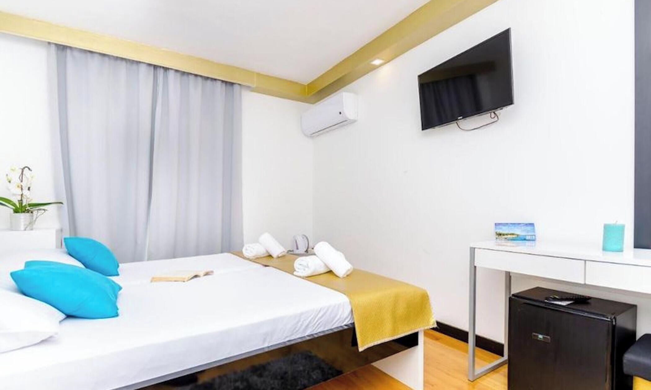 Una habitación de hotel con cama, escritorio, televisión y un refrigerador pequeño.
