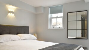 Une chambre à coucher avec un grand lit, une tête de lit, une lampe de chevet, une fenêtre donnant sur un beau paysage et un miroir fixé au mur.