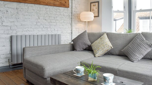 Un salon chaleureux avec un canapé gris, un panneau en bois accroché au mur, une lampe sur pied et une table basse agrémentée d’objets décoratifs.