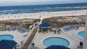 A beach view from a resort with two swimming pools, lounge chairs, and a wooden deck. - Cozy Beach Condo with Private Beach, heated pool, High Speed WiFi, and More. (Orange Beach)