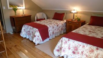 A bedroom with two beds, wooden flooring, a mirror, a dresser, and a chair.