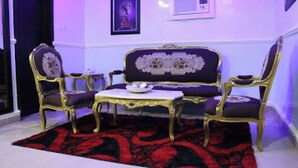 A room with a sofa, two chairs, a small table, and a red patterned rug. - Room-all Seasons Hotel-apartment (Owerri)