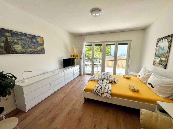 Um quarto com cama, televisão, quadro e varanda.