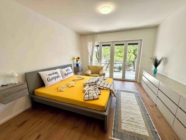 A bedroom with a bed, bedside table, lamp, and a view of the outdoors through a sliding door.