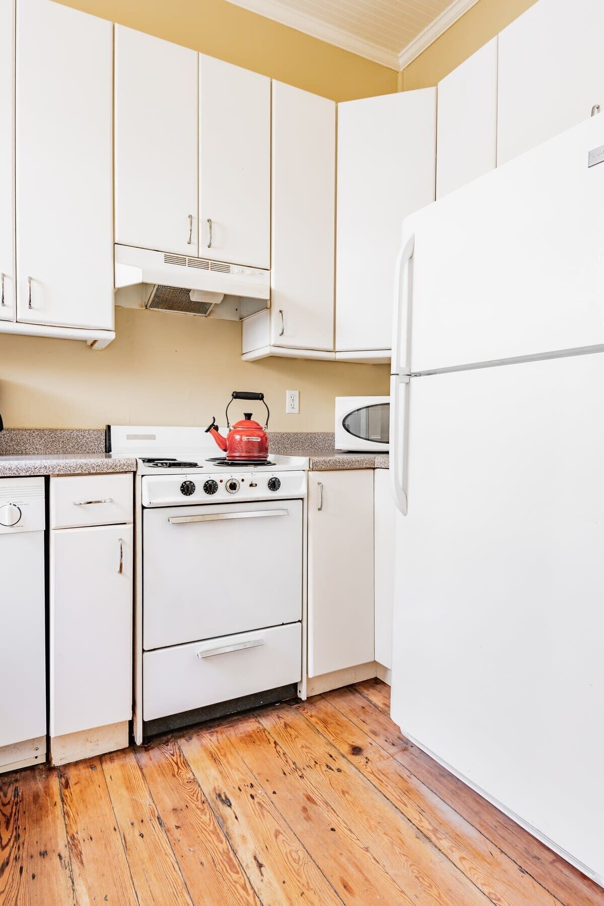 Una cocina con gabinetes blancos, estufa, microondas y refrigerador.