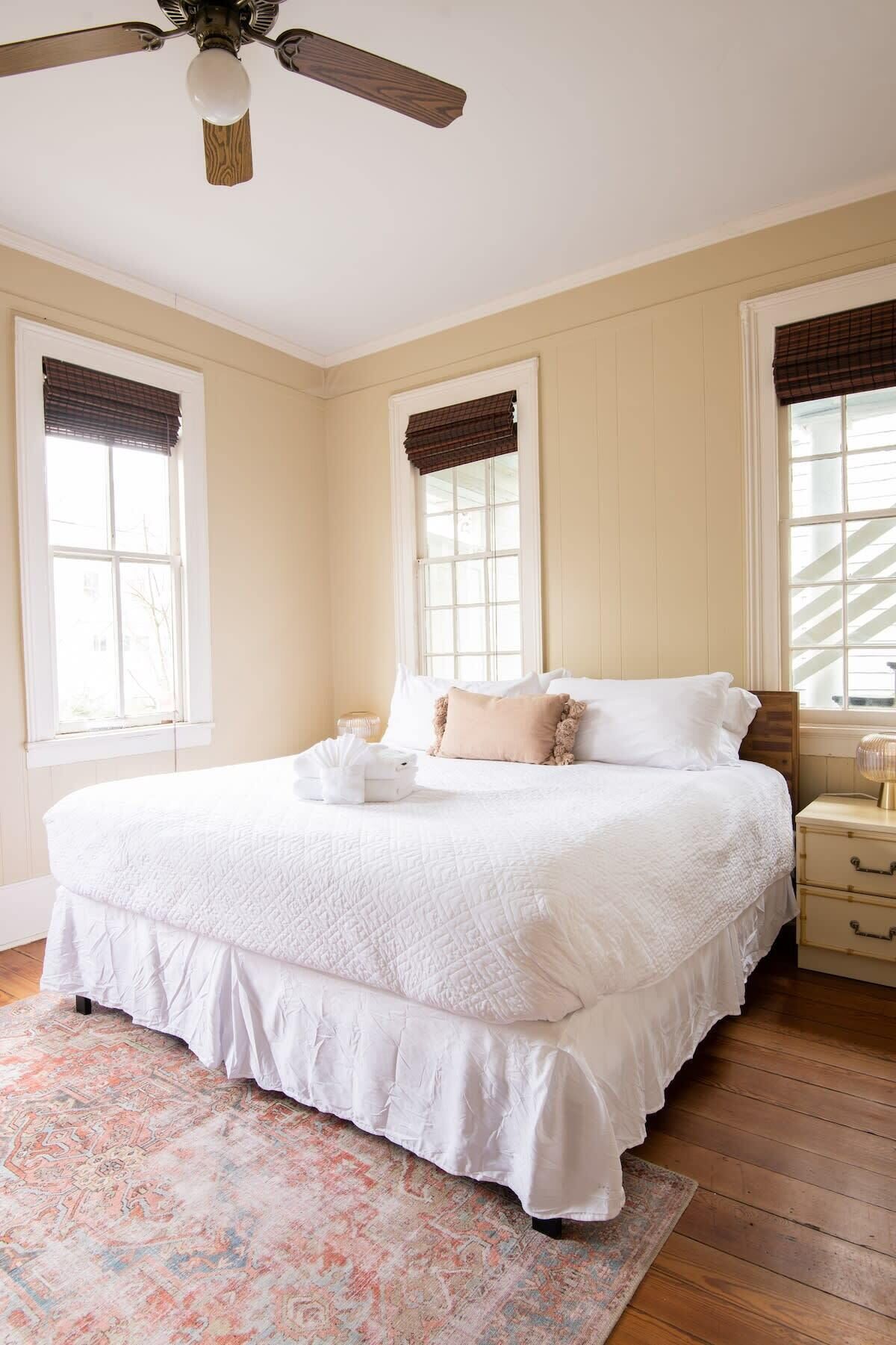 A bedroom with a large bed, two bedside tables, a ceiling fan, and a window with a plaid blind.