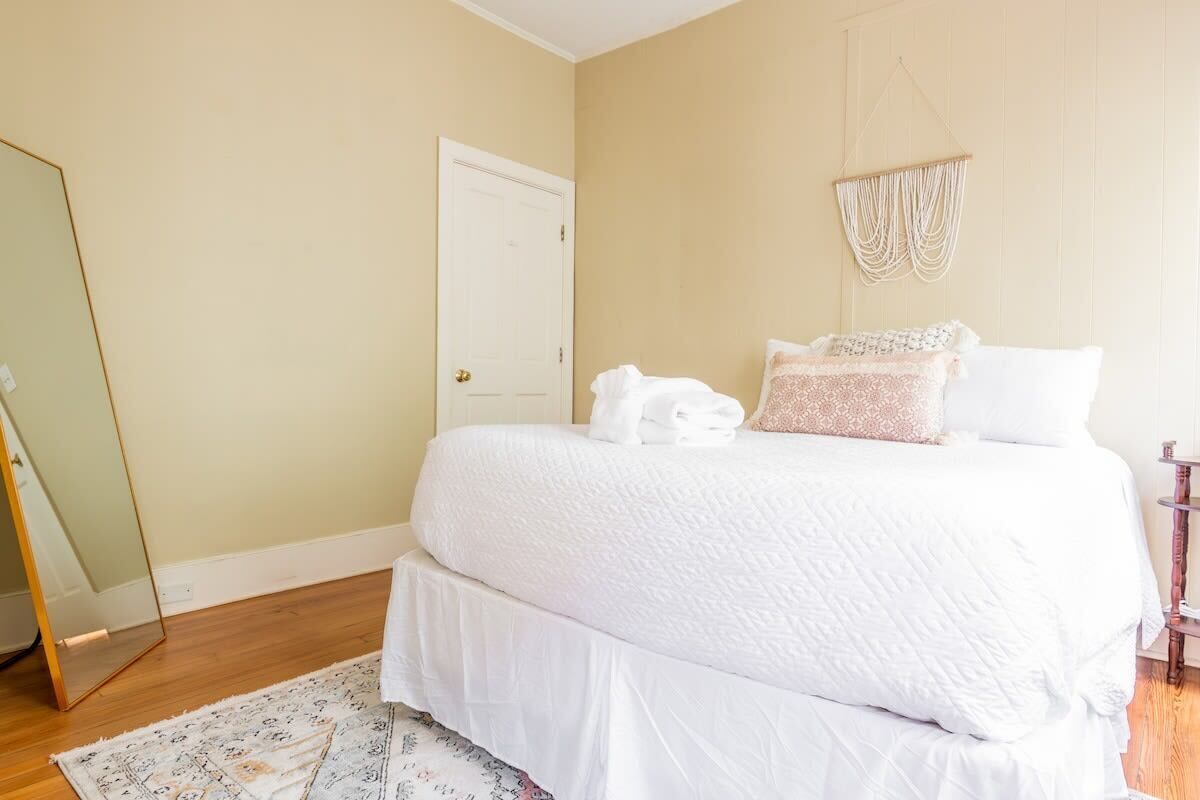A bedroom with a bed, a mirror, and a macrame wall hanging.