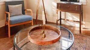 A living room with a glass coffee table, a blue armchair, a floor lamp, a wooden side table with a TV, and a ceiling fan.