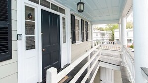 A covered porch with a black door, white railings, and a hanging lantern. - Historic Charleston Charm (Charleston)