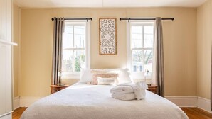 A neatly made bed with a white comforter and a 'Charleston' pillow, two bedside tables with lamps, and a window with curtains. - Historic Charleston Charm (Charleston)