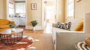 A living room with a sofa, a coffee table, a cowhide rug, and a kitchen in the background. - Historic Charleston Charm (Charleston)