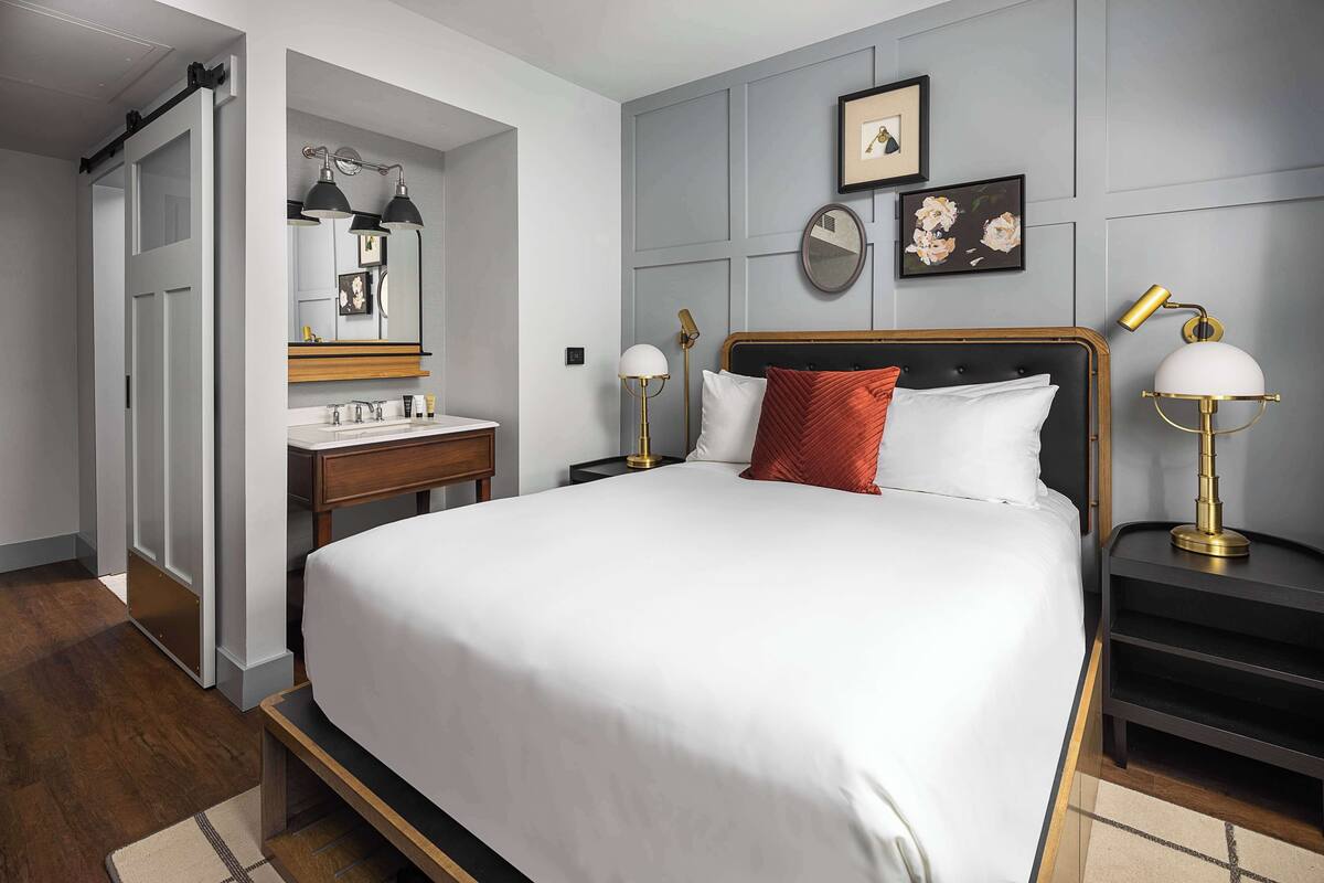 A bedroom with a large bed, a wooden nightstand, a bedside table, a mirror, and a wall-mounted lamp.