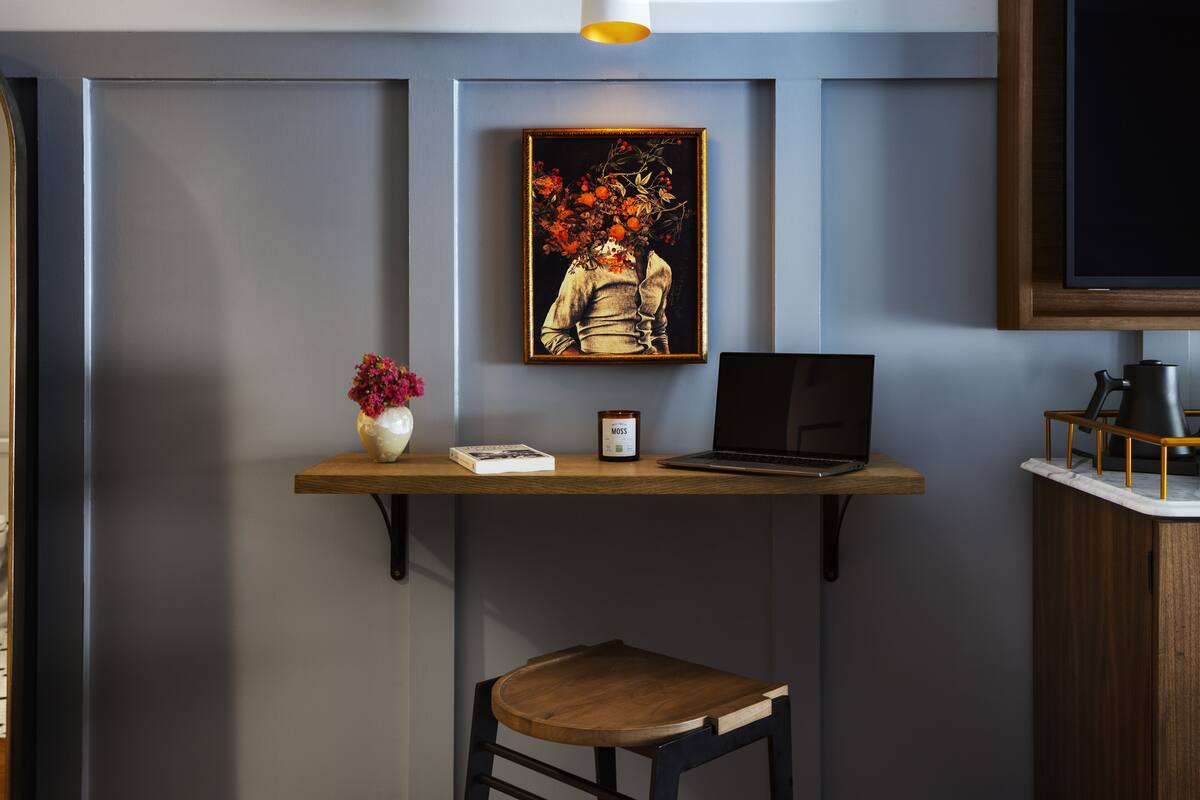 A modern workspace with a laptop, a small table with a vase of flowers, and a framed artwork on the wall.